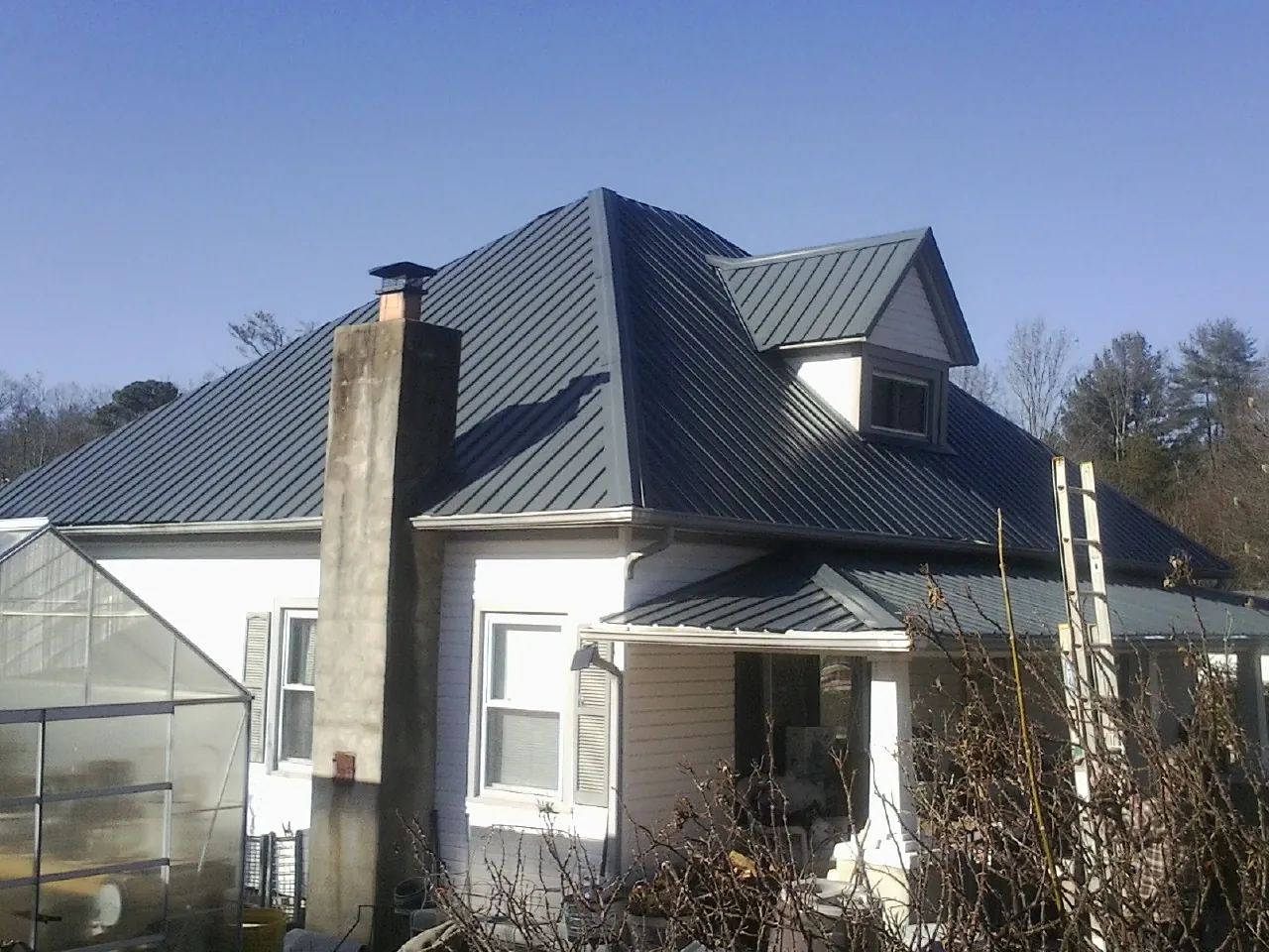 Dark blue standing seam metal roof on a white farmhouse with dormer — Slate & Tile Roof Repair by Roofing Brothers in Ellington