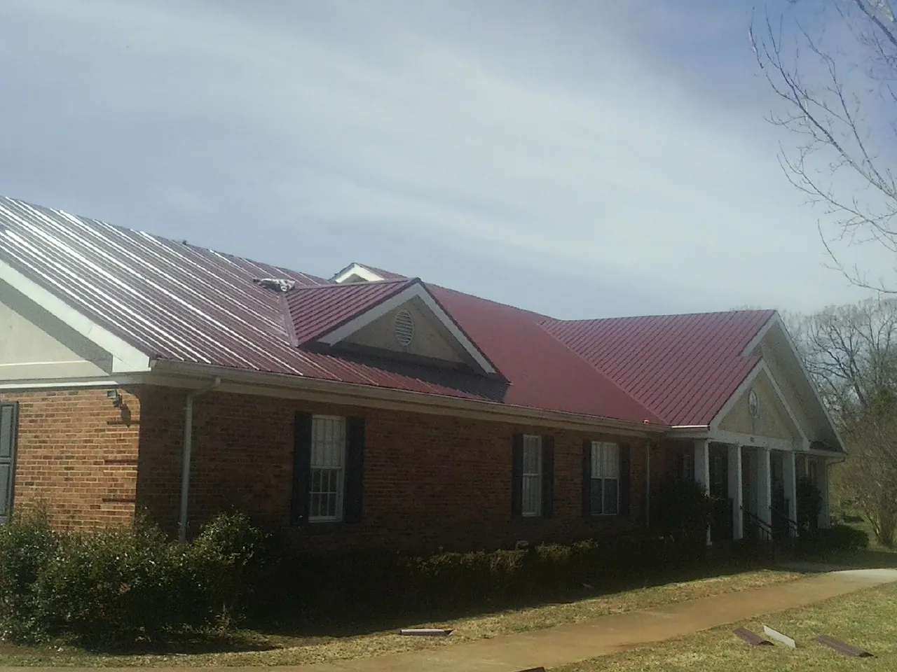 Red metal roof with gabled entries on a long brick building, from a Hail Damage Roof Repair job in Ellington