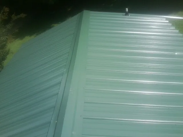 New green metal panels meeting at the ridge of a roof — Flat Roof Repair work by our crew in Ellington
